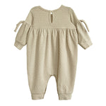 The Cinnamon Sugar Romper by Mabel and Honey is a beige, long-sleeve baby girl romper with textured fabric, a gathered waist, bow-tied sleeves, back button closure, and cuffed ankles for a sweet and comfy fit.