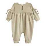 The Cinnamon Sugar Romper by Mabel and Honey is a beige, long-sleeve baby girl romper with textured fabric, a gathered waist, bow-tied sleeves, back button closure, and cuffed ankles for a sweet and comfy fit.