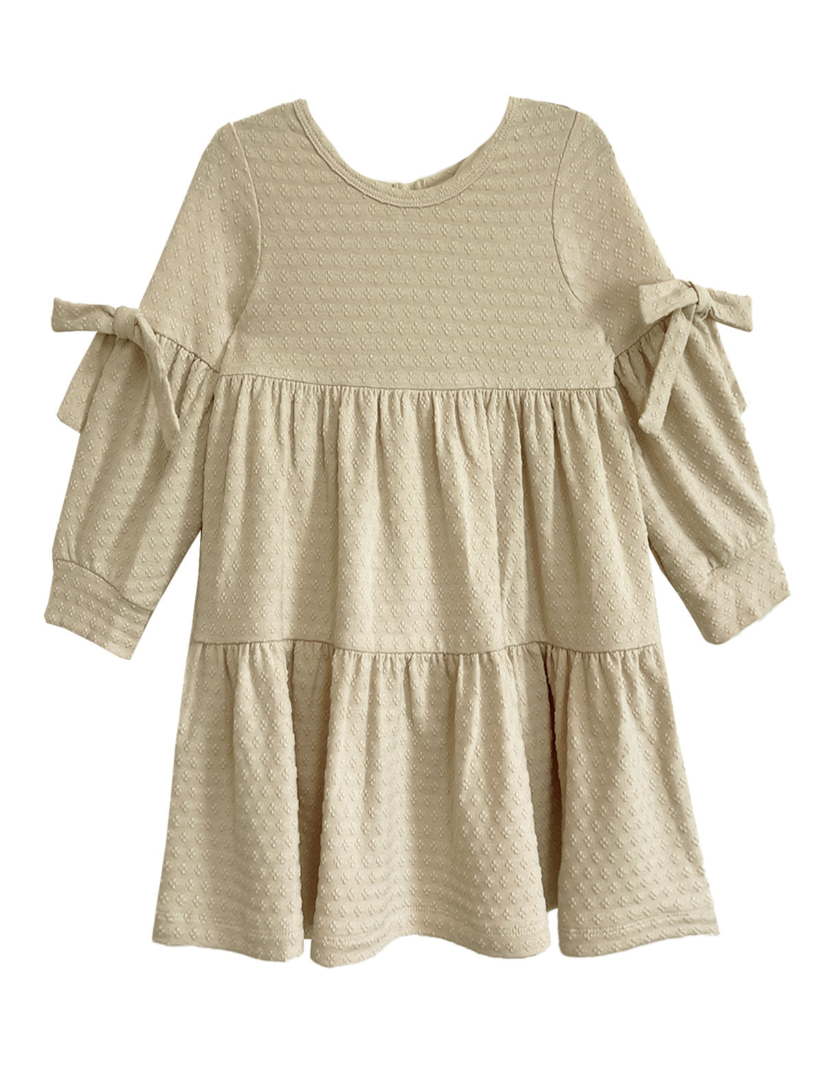 The Mabel and Honey Cinnamon Sugar Dress is a cream-colored toddler dress with textured fabric, a tiered silhouette, long sleeves, and decorative bows on each sleeve.