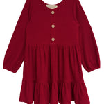 The Mabel and Honey Rosie Dress is a red, long-sleeve girl’s dress with ribbed fabric, wooden front buttons, a round neckline, and a gathered ruffled skirt.