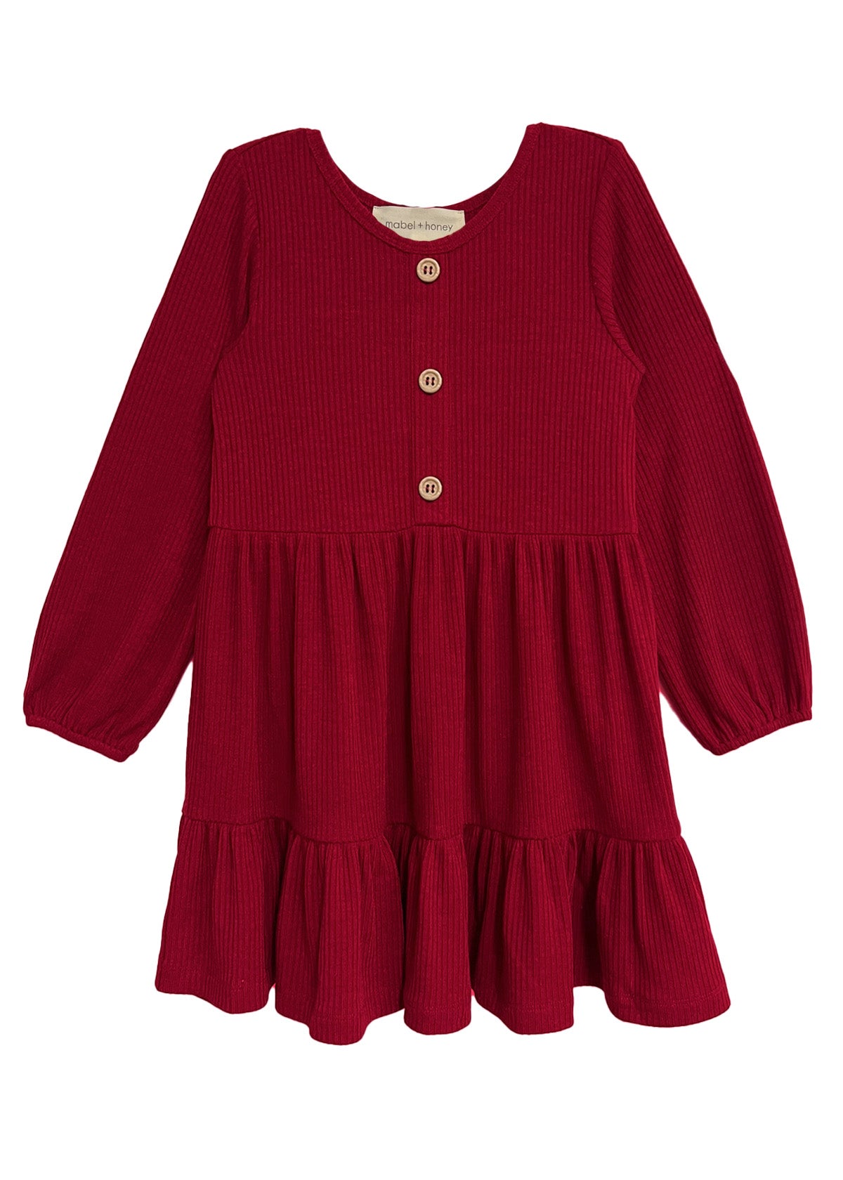The Mabel and Honey Rosie Dress is a red, long-sleeve girl’s dress with ribbed fabric, wooden front buttons, a round neckline, and a gathered ruffled skirt.
