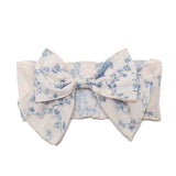 The Isobella and Chloe Princess Hair Accessory is a wide cream headband with a textured, gathered design and a large blue floral bow, adding elegant charm to any girls outfit.
