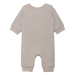 The Beckett and Bear Isaac Romper is a light beige, neutral-tone one-piece with cuffed sleeves and legs. Shown flat from the back, its simple solid design has no visible patterns or decorations.