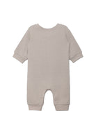The Beckett and Bear Isaac Romper is a light beige, neutral-tone one-piece with cuffed sleeves and legs. Shown flat from the back, its simple solid design has no visible patterns or decorations.