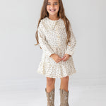 A young girl with long brown hair smiles against a white background, wearing the Mabel and Honey Juliette Two Piece Set and tan cowboy boots.
