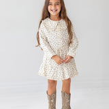 A young girl with long brown hair smiles against a white background, wearing the Mabel and Honey Juliette Two Piece Set and tan cowboy boots.