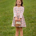 A young girl smiles on the grass, wearing the Mabel and Honey Phoebe Dress with long sleeves and holding a basket of white flowers.