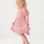 A young girl with blonde hair smiles in the Isobella and Chloe Glitter and Glitz Dress, posing against a plain white background.