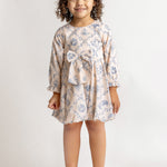A young girl with curly hair smiles against a plain background, wearing the Mabel and Honey Princess Dress—a blue floral long-sleeve dress with a bow—paired with white shoes for a charming princess look.