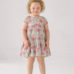 A girl wears the Mabel and Honey April Cap Sleeve Dress, featuring a floral print and a tiered skirt.