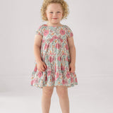 A girl wears the Mabel and Honey April Cap Sleeve Dress, featuring a floral print and a tiered skirt.