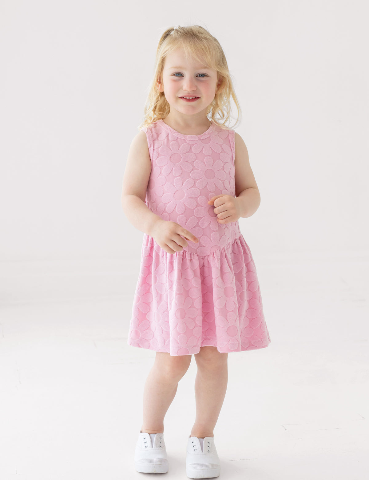 A young child with blonde hair smiles against a white background, wearing the Mabel and Honey Tilly Short Sleeve Dress and white sneakers.
