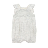 The Mabel and Honey Opal Short Flutter Sleeve Romper features a white floral print, smocked bodice, ruffled shoulder straps, and gathered leg openings for infants, shown on a plain white background.