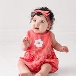 A curly-haired baby wears a Mabel and Honey Striped Blossom Sleeveless Romper with a matching headband, sitting barefoot on a white floor and gazing slightly upward.