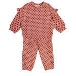 The Red Velvet Two Piece Set by Mabel and Honey is a soft knit toddler outfit with a long-sleeve ruffled top and matching pink pants decorated with red polka dots.