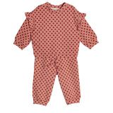 The Red Velvet Two Piece Set by Mabel and Honey is a soft knit toddler outfit with a long-sleeve ruffled top and matching pink pants decorated with red polka dots.