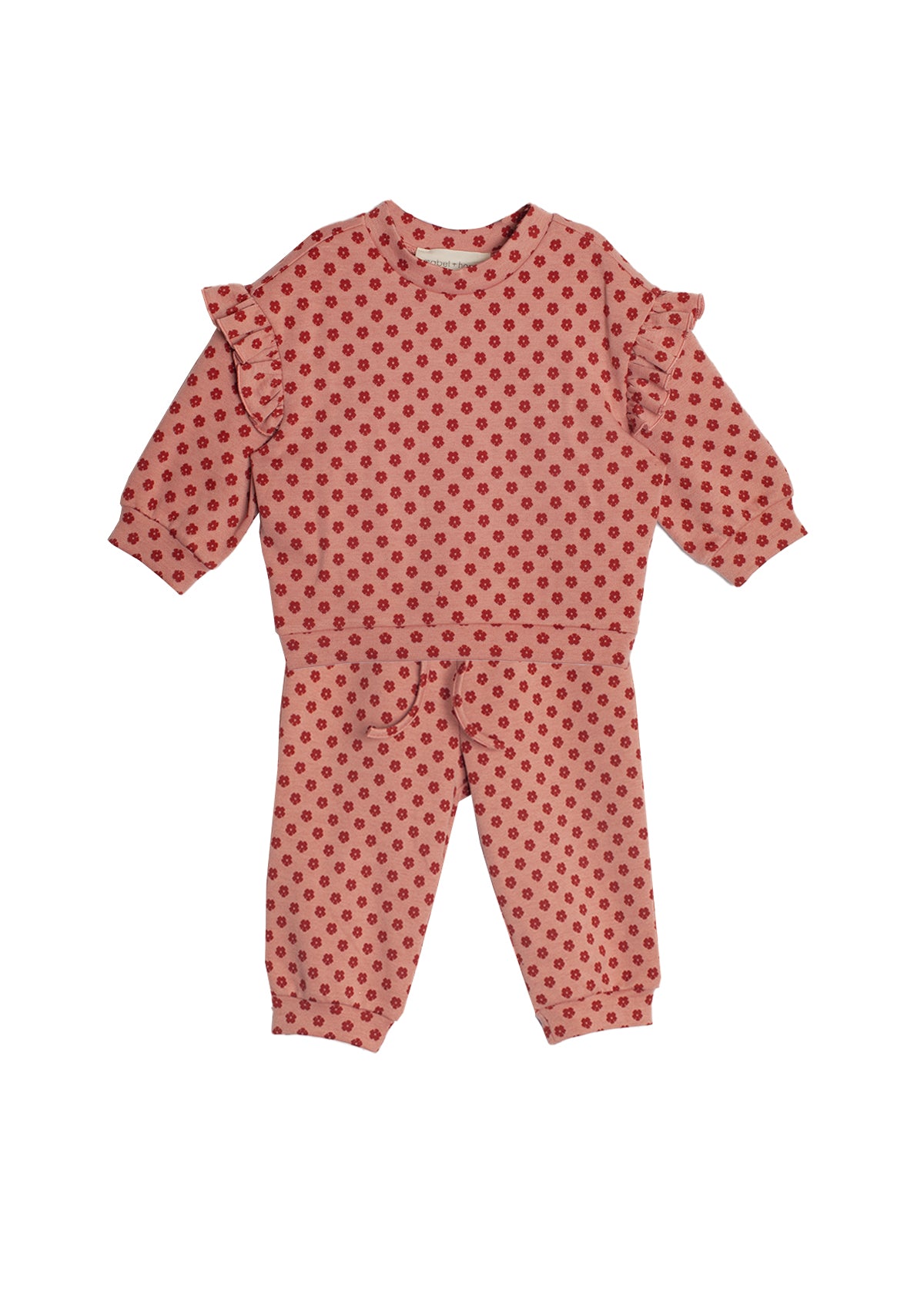 The Red Velvet Two Piece Set by Mabel and Honey is a soft knit toddler outfit with a long-sleeve ruffled top and matching pink pants decorated with red polka dots.