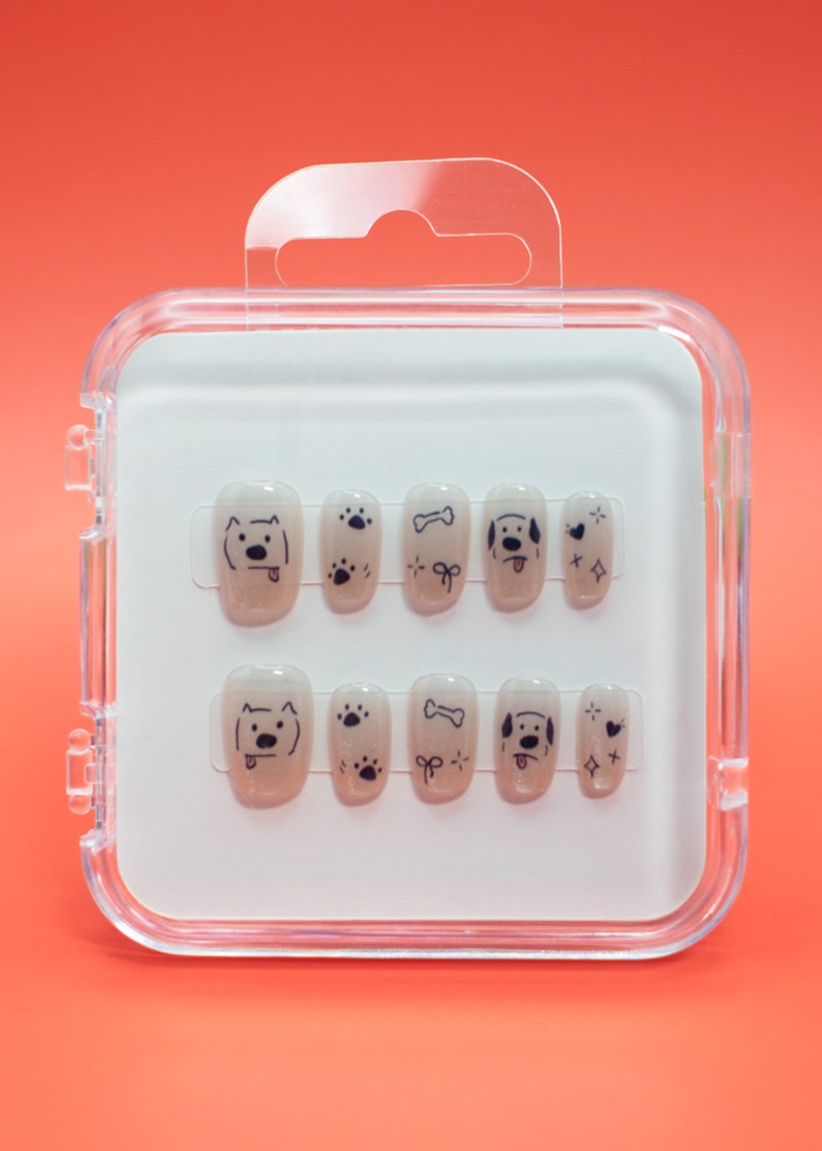 Paw-fection by Mabel and Honey: salon-quality press-on nails in a clear case, each with black dog faces, bones, paw prints, and stars on a nude background—all set against an orange backdrop.