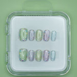 Mabel and Honey’s Confetti set features pastel green, purple, and blue salon-quality press-on nails with iridescent holographic accents, displayed in a clear case against a matching green background.