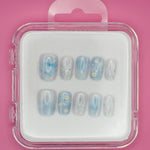 Darling Daisies by Mabel and Honey features blue reusable press-ons with white flower designs and black speckles, shown in a clear plastic case against a pink background.