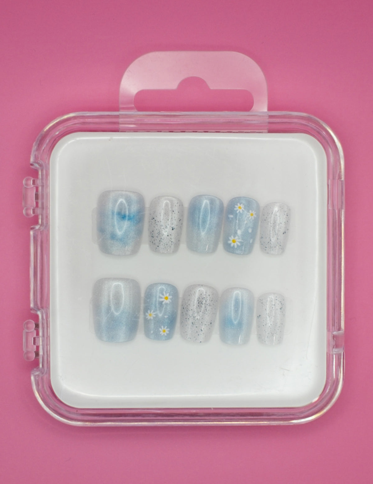 Darling Daisies by Mabel and Honey features blue reusable press-ons with white flower designs and black speckles, shown in a clear plastic case against a pink background.