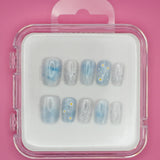 Darling Daisies by Mabel and Honey features blue reusable press-ons with white flower designs and black speckles, shown in a clear plastic case against a pink background.