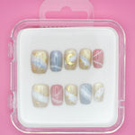 Sweet Dreams by Mabel and Honey: a set of 10 salon-quality press-on nails with pastel blue, pink, and beige swirls, gold stars, moons, and abstract lines. Reusable manicure in a clear case on a pink background.