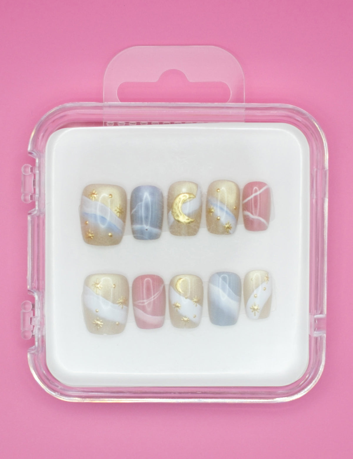 Sweet Dreams by Mabel and Honey: a set of 10 salon-quality press-on nails with pastel blue, pink, and beige swirls, gold stars, moons, and abstract lines. Reusable manicure in a clear case on a pink background.