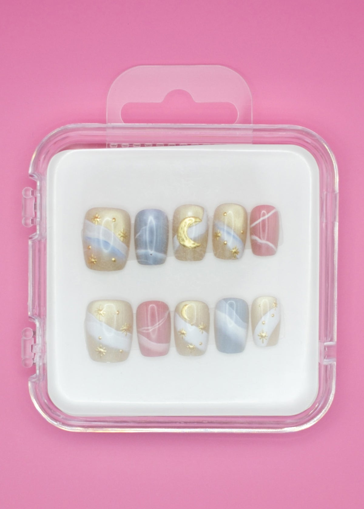 Sweet Dreams by Mabel and Honey: a set of 10 salon-quality press-on nails with pastel blue, pink, and beige swirls, gold stars, moons, and abstract lines. Reusable manicure in a clear case on a pink background.