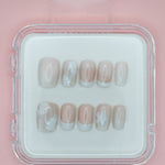 Mabel and Honey's White Floral press-on nails come in a clear case, featuring a pale pink base with white floral details and French tips, displayed on a light pink background.