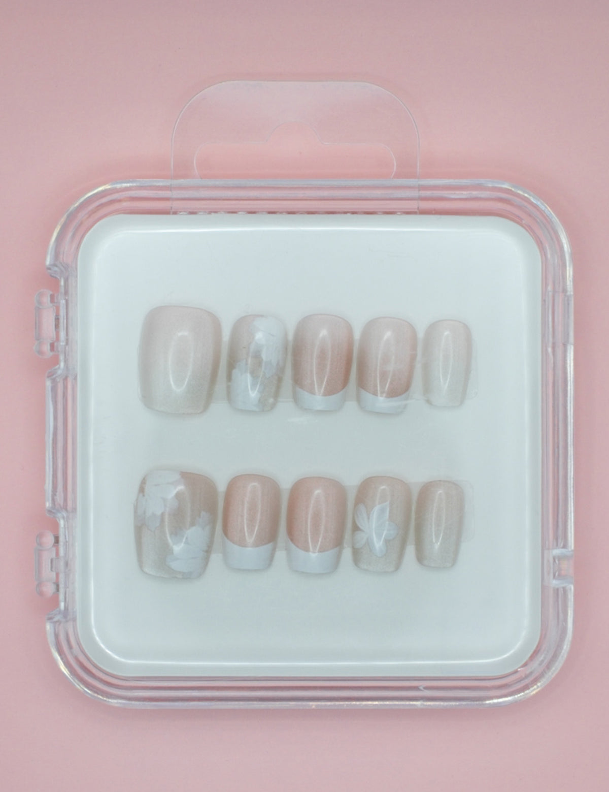 Mabel and Honey's White Floral press-on nails come in a clear case, featuring a pale pink base with white floral details and French tips, displayed on a light pink background.