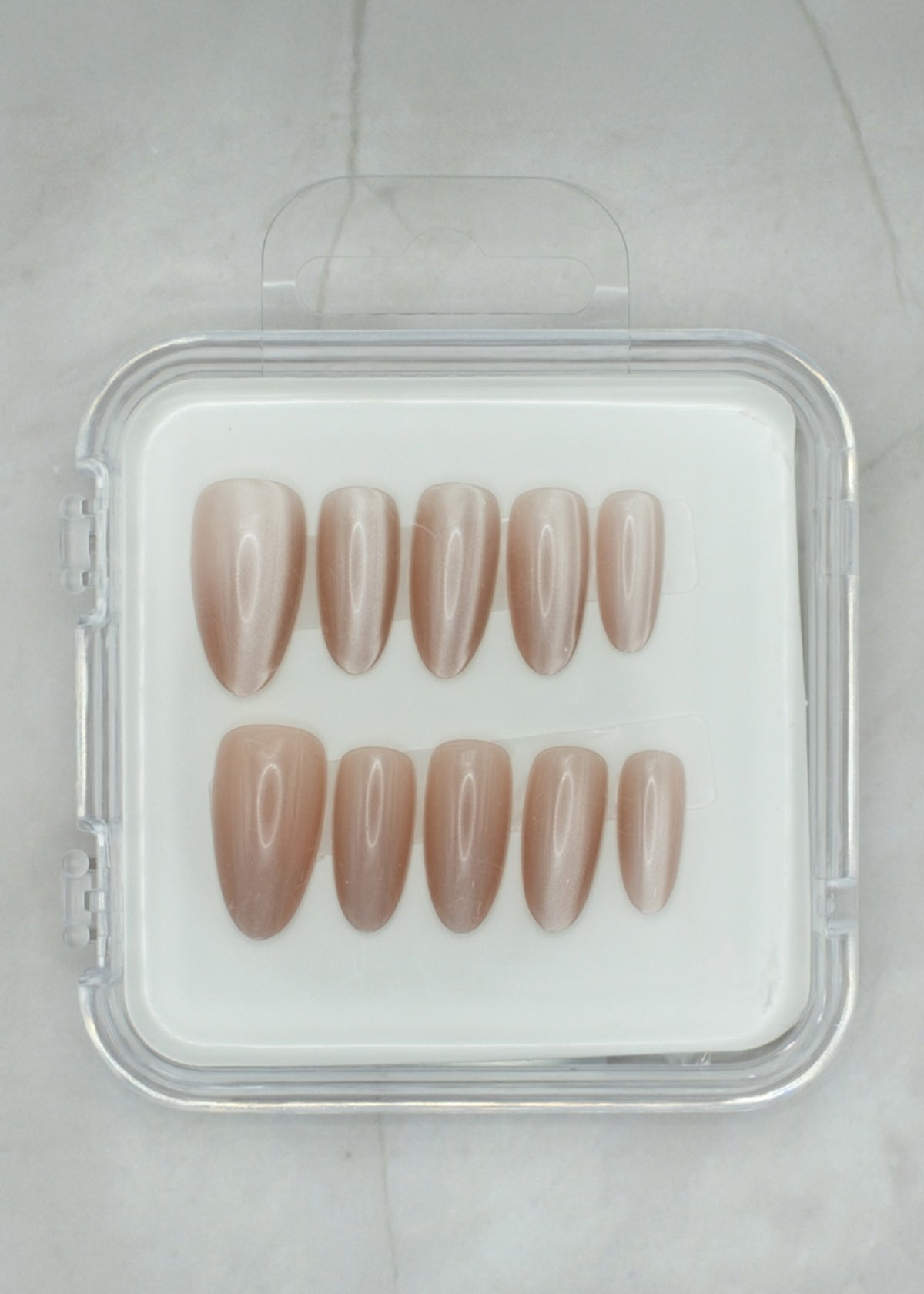 Sheer Delight by Mabel and Honey features ten glossy, almond-shaped nude press-on nails in a clear case, arranged in two rows on a light surface—perfect for achieving a salon-quality manicure at home.