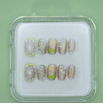 Lemonade by Mabel and Honey: reusable press-on nails in a clear case, featuring fruit designs like lemons and limes for a fun, salon-quality manicure on a vibrant green background.