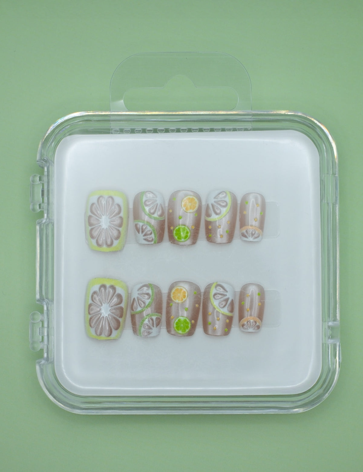 Lemonade by Mabel and Honey: reusable press-on nails in a clear case, featuring fruit designs like lemons and limes for a fun, salon-quality manicure on a vibrant green background.
