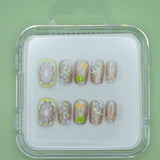 Lemonade by Mabel and Honey: reusable press-on nails in a clear case, featuring fruit designs like lemons and limes for a fun, salon-quality manicure on a vibrant green background.