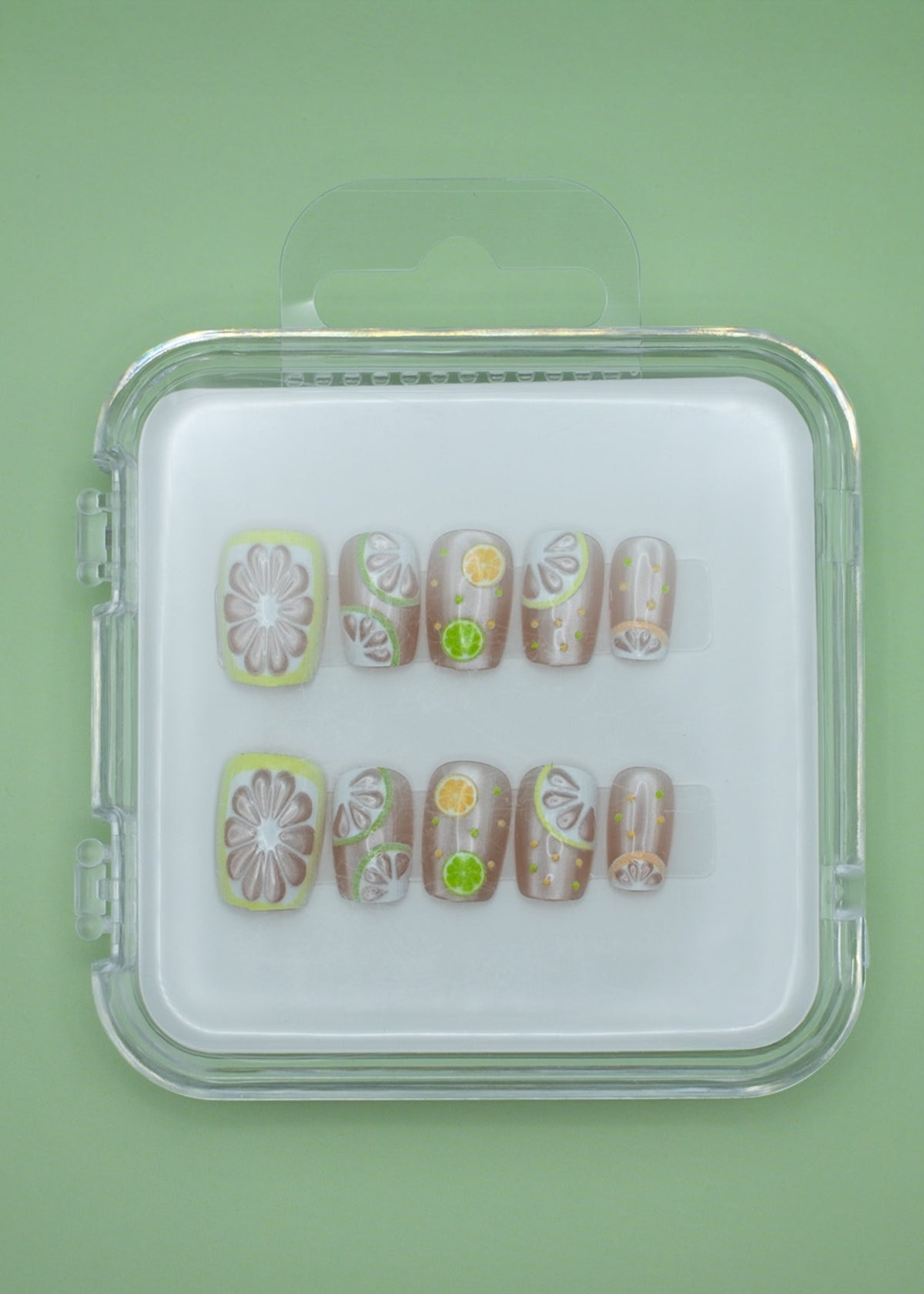 Lemonade by Mabel and Honey: reusable press-on nails in a clear case, featuring fruit designs like lemons and limes for a fun, salon-quality manicure on a vibrant green background.