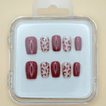Wild Thing by Mabel and Honey is a set of salon-quality, reusable press-on nails in a plastic case, featuring solid burgundy and beige with burgundy leopard spots, all neatly arranged in two rows.