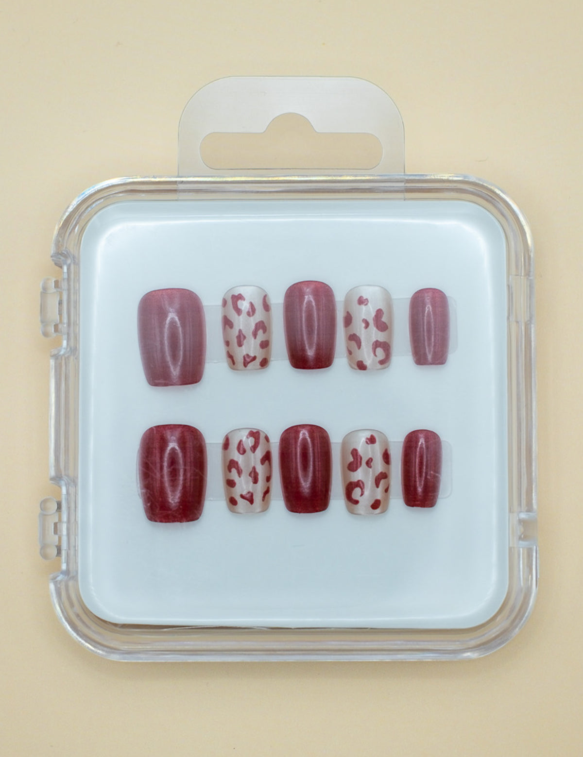 Wild Thing by Mabel and Honey is a set of salon-quality, reusable press-on nails in a plastic case, featuring solid burgundy and beige with burgundy leopard spots, all neatly arranged in two rows.