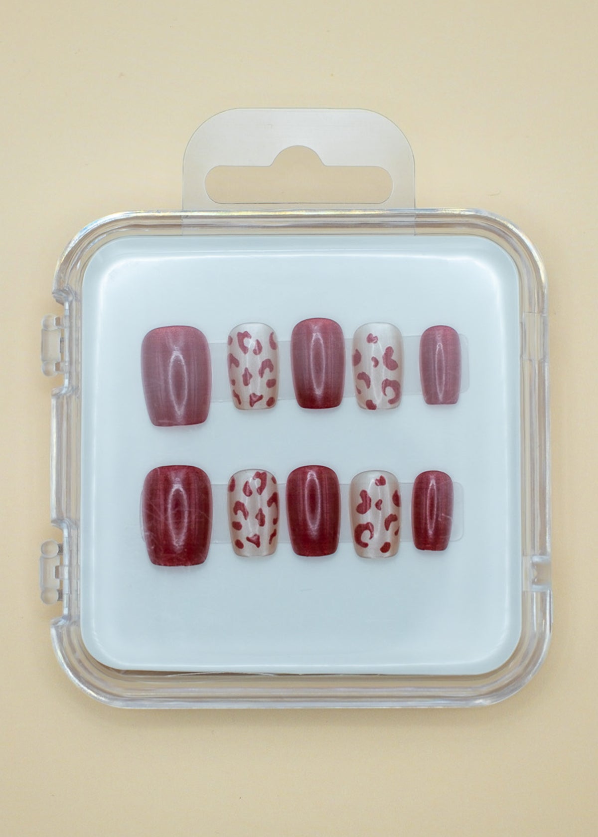 Wild Thing by Mabel and Honey is a set of salon-quality, reusable press-on nails in a plastic case, featuring solid burgundy and beige with burgundy leopard spots, all neatly arranged in two rows.