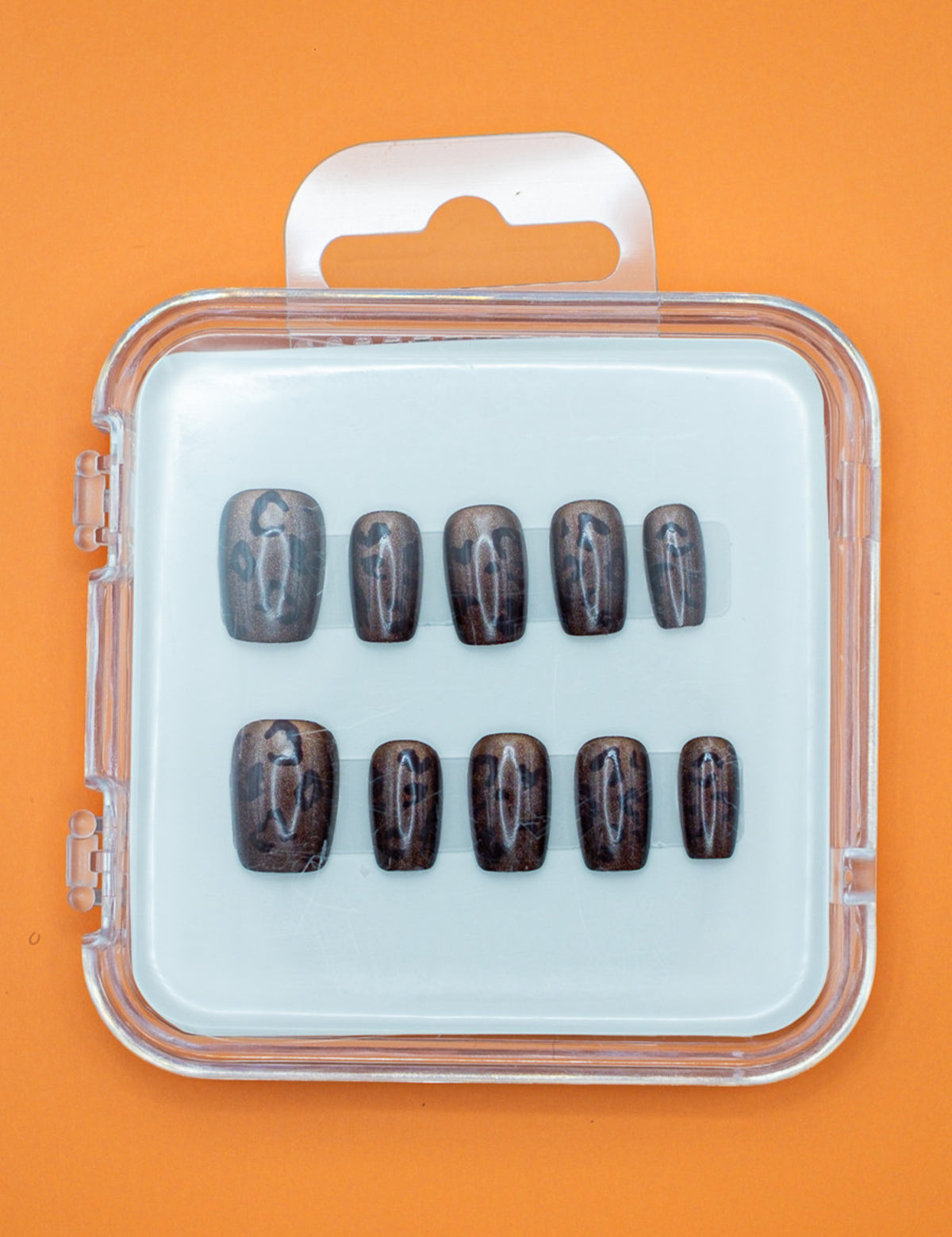 Cheetah Chic by Mabel and Honey features ten glossy, dark brown press-on nails in assorted sizes, arranged in a clear plastic case with a white insert and orange background for a salon-quality manicure at home.
