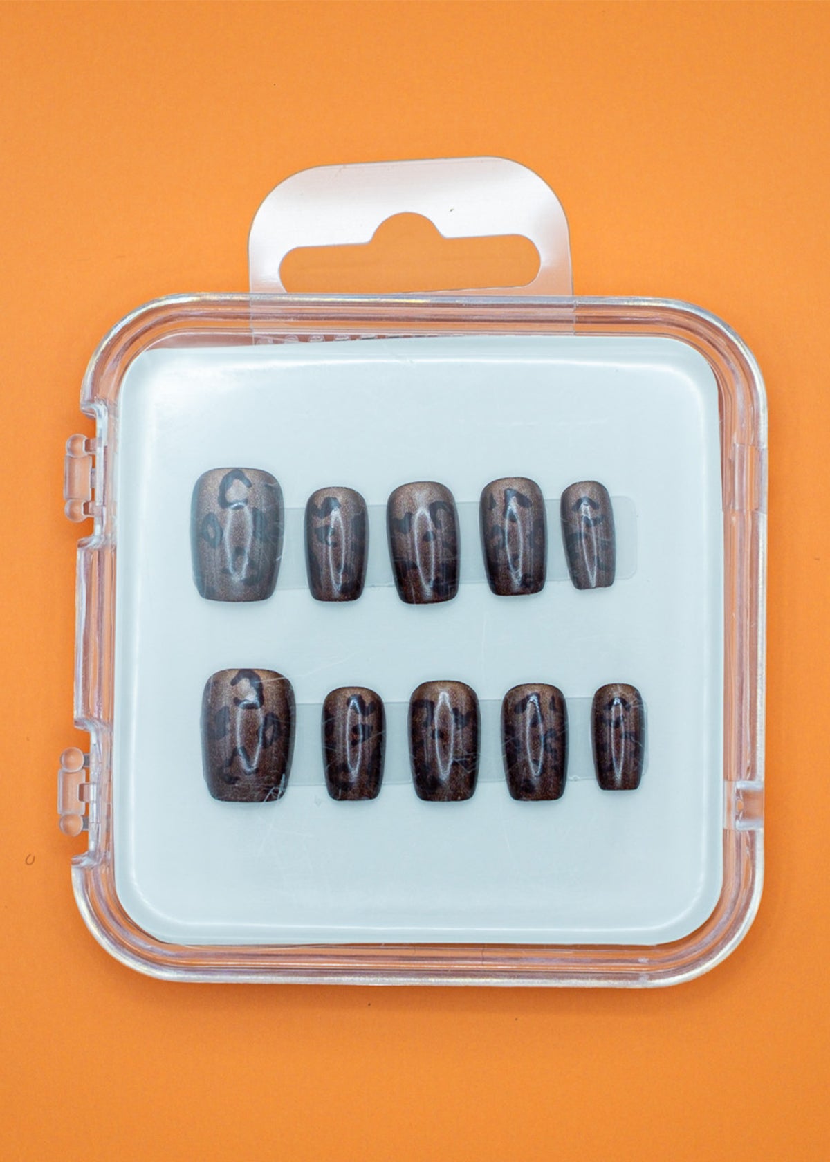 Cheetah Chic by Mabel and Honey features ten glossy, dark brown press-on nails in assorted sizes, arranged in a clear plastic case with a white insert and orange background for a salon-quality manicure at home.