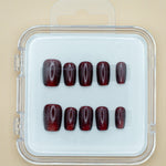 Red Amber by Mabel and Honey features ten dark red, glossy press-on nails arranged in two rows inside a clear case, perfect for achieving a salon-quality manicure at home.