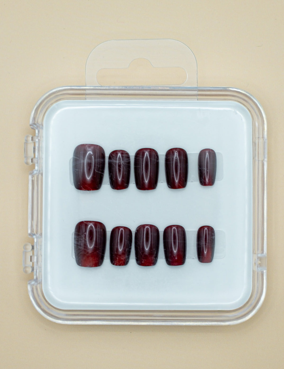 Red Amber by Mabel and Honey features ten dark red, glossy press-on nails arranged in two rows inside a clear case, perfect for achieving a salon-quality manicure at home.