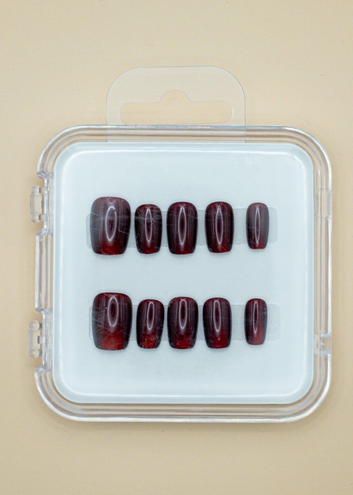 Red Amber by Mabel and Honey features ten dark red, glossy press-on nails arranged in two rows inside a clear case, perfect for achieving a salon-quality manicure at home.