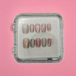 Wish You Well Acrylic Nails by Mabel and Honey come in a clear square case, featuring a shiny nude design with white lines, bows, and small flowers for a salon-quality manicure at home. Displayed on a light pink background.