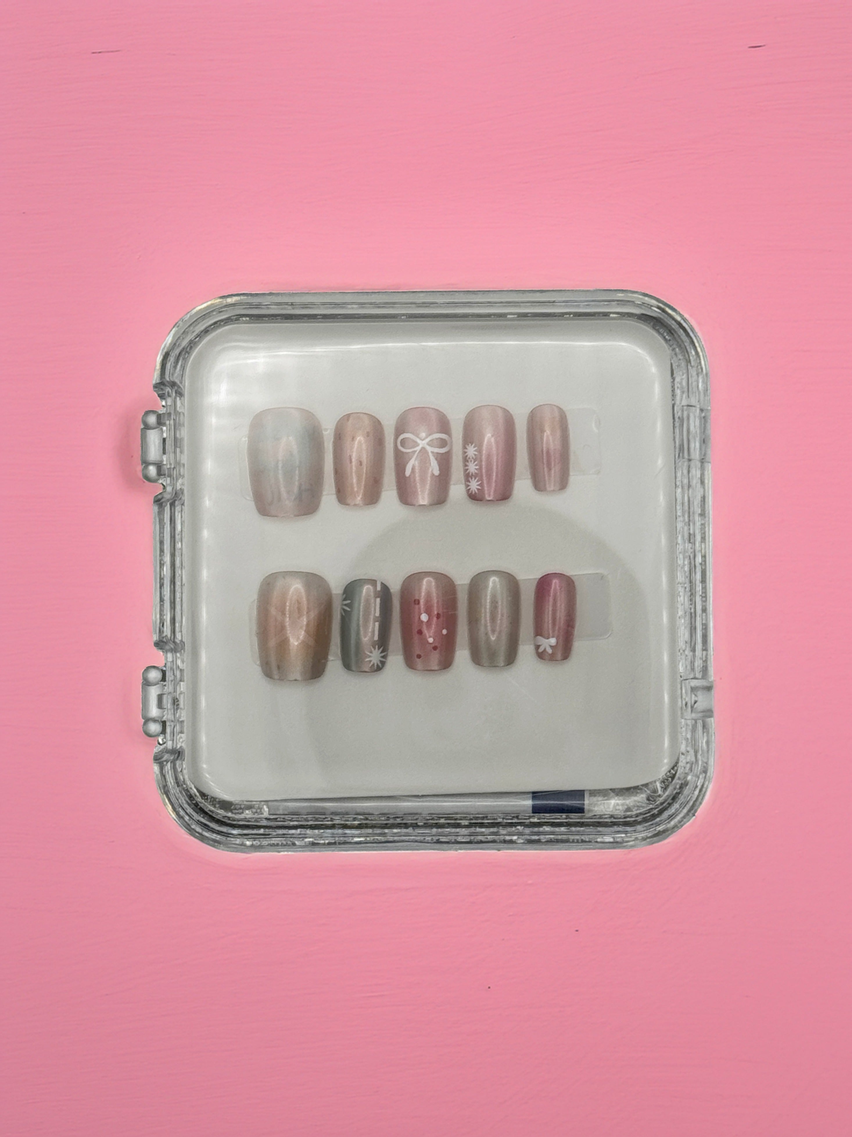 Wish You Well Acrylic Nails by Mabel and Honey come in a clear square case, featuring a shiny nude design with white lines, bows, and small flowers for a salon-quality manicure at home. Displayed on a light pink background.