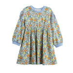 The Mabel + Honey Ivy Bloom Dress is a long-sleeve children’s dress featuring a colorful floral and leaf pattern, light blue cuffs and neckline, as well as charming ribbon bows on the sleeve slits and a gathered skirt.