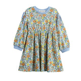 The Mabel + Honey Ivy Bloom Dress is a long-sleeve children’s dress featuring a colorful floral and leaf pattern, light blue cuffs and neckline, as well as charming ribbon bows on the sleeve slits and a gathered skirt.
