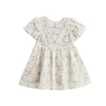 Introducing the Mabel + Honey Golden Goose Dress Short Sleeve Floral Fit And Flare Dress: a cream-colored baby dress featuring short puffed sleeves, a round neckline, and an elegant floral lace overlay. With its flared skirt and intricate embroidered details throughout, this charming holiday party dress is perfect for any special occasion. Displayed on a white background.