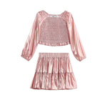 The Rosy Glow Two Piece Set by Mabel + Honey features a shiny pink metallic rose gold long-sleeve smocked crop top with gathered detailing, paired with a matching tiered skirt adorned with playful ruffles.
